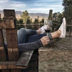 a person sitting on a wooden bench holding a wine glass with their feet in the air