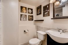 a white toilet sitting next to a sink in a bathroom under pictures on the wall