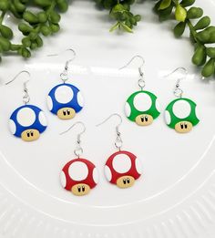 four pairs of nintendo mushroom earrings on a white plate next to some green plants and leaves