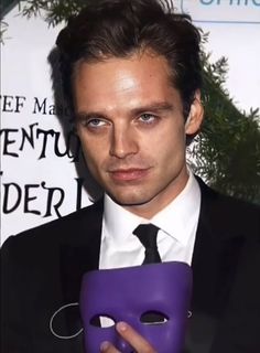 a man in a suit holding a purple mask