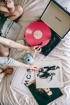 two people sitting on a bed next to an open laptop and a red record player