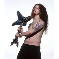 a shirtless man with long hair holding a guitar in his right hand and looking at the camera