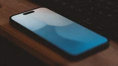 an iphone sitting on top of a wooden table next to a keyboard