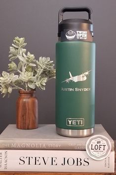 a green yeti water bottle sitting on top of a stack of books next to a potted plant