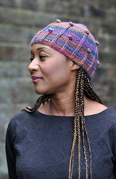 a woman with braids wearing a multicolored knitted hat and looking off to the side