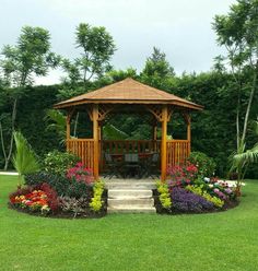 a wooden gazebo sitting in the middle of a lush green field next to flowers