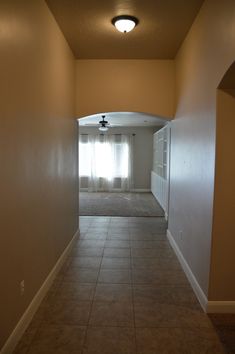 an empty room with tile flooring and ceiling fan in the corner, leading into another room