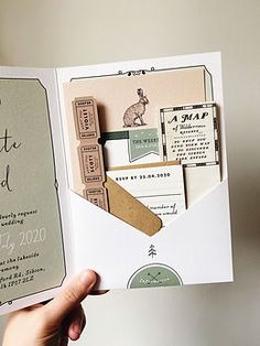 a hand holding an open book that has some paper on it and the words save the date