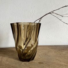 a glass vase sitting on top of a table next to a twig in front of a white wall