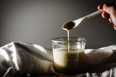 a spoon pouring liquid into a glass jar on top of a cloth covered tablecloth