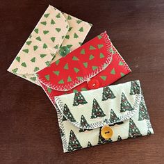 three small envelopes with christmas trees on them sitting on top of a wooden table