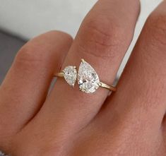 a woman's hand with a diamond ring on top of her finger and two pear shaped diamonds in the middle