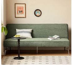 a green couch sitting next to a table on top of a hard wood floored floor