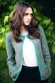 a woman standing in front of some trees wearing a green and white jacket with blue trim