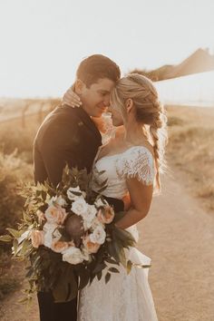 a bride and groom standing on a dirt road