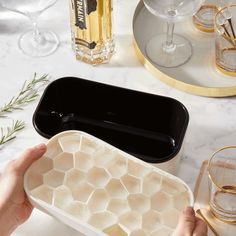 a person is holding an ice tray on a marble table with wine glasses and bottles in the background