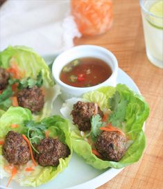 meatballs in lettuce with carrots and sauce on a plate next to a glass of water