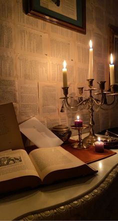 an open book sitting on top of a table next to a candle and some books