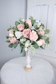 a white vase filled with pink and white flowers on top of a round cloth covered table