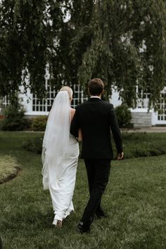 a bride and groom walking through the grass