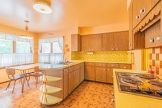 an empty kitchen with yellow counter tops and chairs around the stove top island in the middle