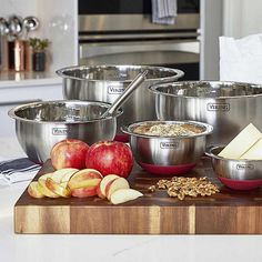 an assortment of stainless steel bowls on a cutting board with apples, oatmeal and other ingredients