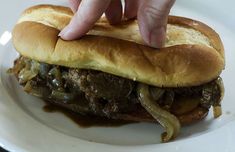 a hand reaching for a sandwich on a plate with onions and meat in the middle