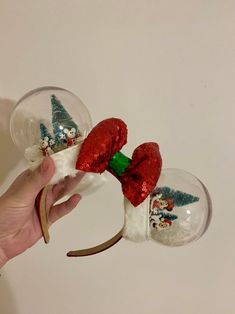 a hand is holding two snow globes with santa hats and bows on them,