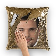 a person holding their hand up to a gold sequin pillow with a man's face on it