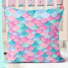 a pink and blue pillow sitting on top of a white bed next to a crib