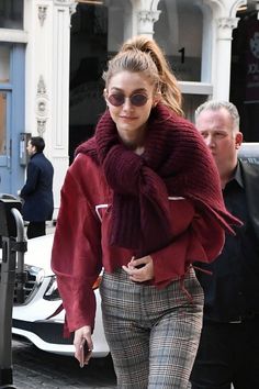 a woman in red sweater and plaid pants walking down the street with her hand on her hip