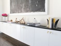 a black and white painting is on the wall above a shelf with books, vases and other items