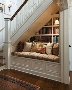 a window seat under a staircase with bookshelves and pillows on the bottom shelf