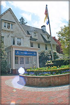 a large white house with a flag on top of it's roof and flowers in the front yard