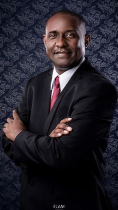 a man in a black suit and red tie posing for a photo with his arms crossed