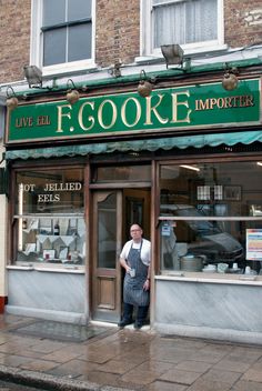 a man standing in front of a store with his hands on his hips while wearing an apron