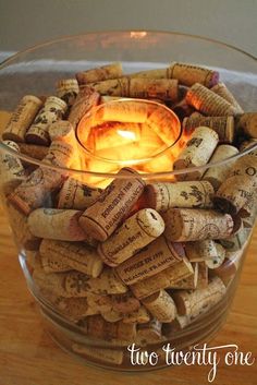 a glass bowl filled with wine corks on top of a wooden table next to a candle