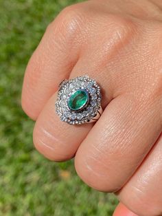 a person's hand holding a ring with an oval shaped emerald and diamond center