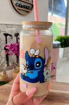 a hand holding a glass with a cartoon character painted on it and a straw in the other hand