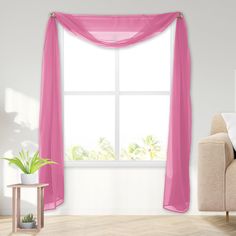 a living room with a couch, chair and large window covered in pink sheer curtains