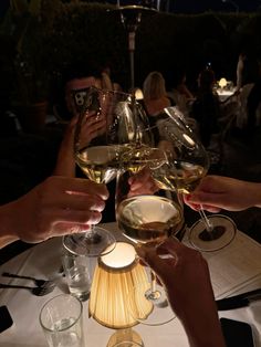 several people are toasting with wine glasses on a table at an outdoor dinner party