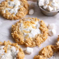 several cookies with marshmallows are on a white surface next to a bowl