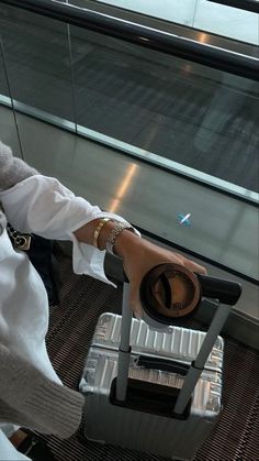 a woman sitting on top of an airport chair next to a luggage bag and looking out the window