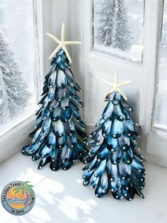 two small blue christmas trees sitting in front of a window