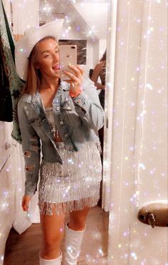 a woman taking a selfie in front of a mirror wearing boots and a fringe skirt