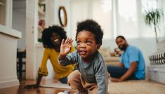 a young child is playing on the floor while his parents are sitting in the background