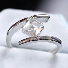 a white gold ring with a princess cut diamond on it's side, sitting on a piece of cloth