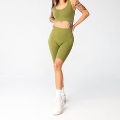 a woman in tight green shorts and cropped tank top posing for the camera with her hands on her hips