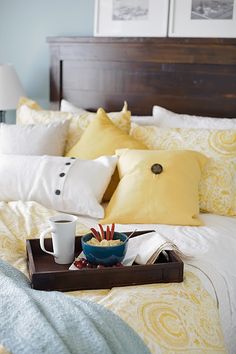 a tray with some food on top of a bed next to pillows and pictures above it