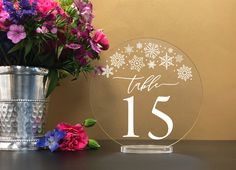 there is a vase with flowers and a table number on it next to a silver cup